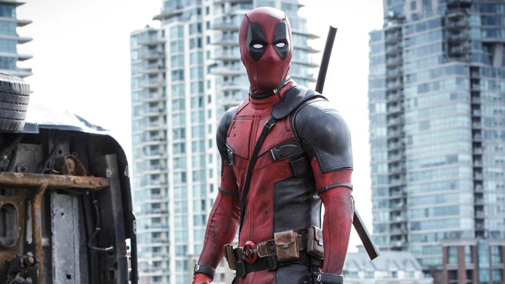 A close-up side profile of the character Deadpool in his signature red and black tactical suit, looking toward the right with a blurred background.