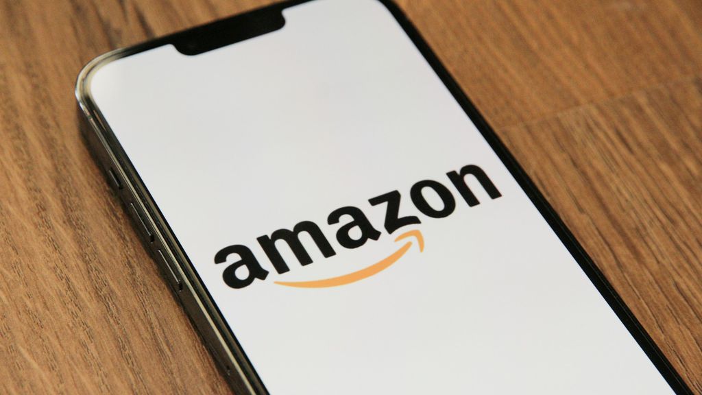 A smartphone on a wooden table displaying the Amazon logo, representing new AI voice shopping features.