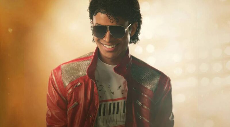An actor with curly hair and sunglasses, looking like Michael Jackson, wears a red jacket over a white shirt with a musical staff pattern.
