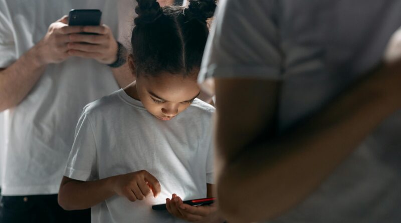 A child with their head down using a smartphone in a line with other children.
