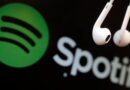 The white Spotify logo on a green background alongside a pair of white wired earphones on a black background.