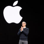 Apple CEO, Tim Cook, standing on stage in front of a large, glowing white Apple logo.
