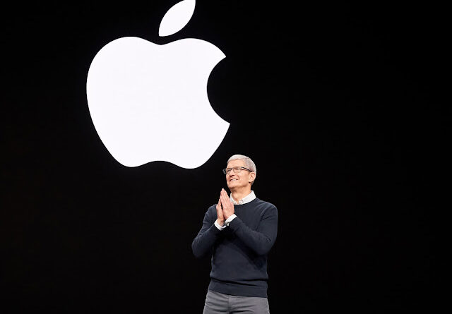 Apple CEO, Tim Cook, standing on stage in front of a large, glowing white Apple logo.