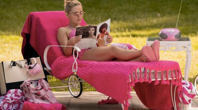 A young woman with blonde hair, wearing pink sunglasses and a pink outfit, lounging on a pink towel-covered chair and reading a magazine outdoors.