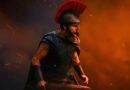 A powerful cinematic shot of a Greek warrior, portrayed by Matt Damon, wearing a black breastplate and a Spartan-style helmet with a large red crest. He is shouting in the heat of battle, holding a sword, amidst a backdrop of orange smoke, embers, and dark shadows.