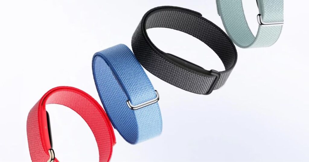 A studio product shot showcasing four Fitbit Air smart bands with woven fabric straps in different colors: vibrant red, bright blue, charcoal black, and pale mint green. The bands are arranged diagonally against a clean white background, highlighting the texture of the fabric and the sleek metallic buckles.