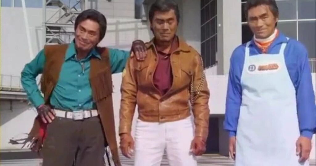 A medium shot of actor Kenji Ohba appearing as three different characters from his most famous roles. To the left, he is dressed as Shiro Akebono (Battle Kenya) in a green shirt and fringed vest; in the center, he appears as Retsu Ichijouji (Gavan) in a classic brown leather jacket and white pants; and to the right, he is depicted as Daigoro Oume (Denzi Blue) wearing a blue shirt and a white apron.