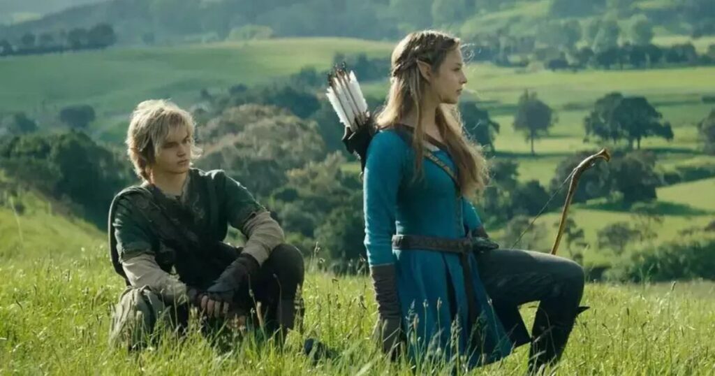 Live-action portrayal of Link and Princess Zelda, played by Benjamin Evan Ainsworth and Bo Bragason, kneeling in a lush green field in a cinematic scene from the upcoming movie.