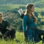 Live-action portrayal of Link and Princess Zelda, played by Benjamin Evan Ainsworth and Bo Bragason, kneeling in a lush green field in a cinematic scene from the upcoming movie.