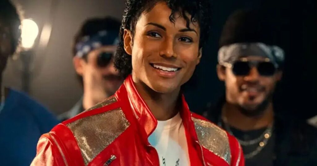 A cinematic still from the biopic Michael. The image features actor Jaafar Jackson in the lead role, wearing a meticulously recreated red and silver jacket synonymous with the Beat It or Thriller era. His performance has been noted for its physical resemblance and capture of the singer's essence. In the background, supporting actors are visible, contributing to the historical atmosphere of the singer's career peak.