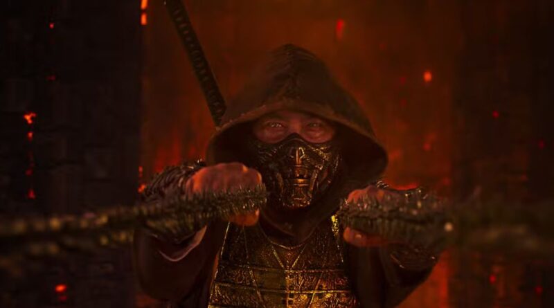 A cinematic close-up of the character Scorpion from Mortal Kombat 2, wearing his iconic gold-detailed mask and dark hood, holding his signature kunai chains forward in a dark, fire-lit environment.
