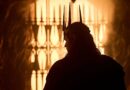 Silhouette of Charlie Vickers as Sauron wearing a spiked crown, standing before a glowing, fiery gate in a scene from The Rings of Power Season 3.