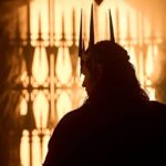 Silhouette of Charlie Vickers as Sauron wearing a spiked crown, standing before a glowing, fiery gate in a scene from The Rings of Power Season 3.